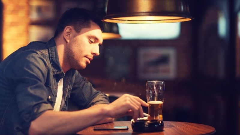 people and bad habits concept - man drinking beer and smoking and shaking off ashes of cigarette at bar or pub