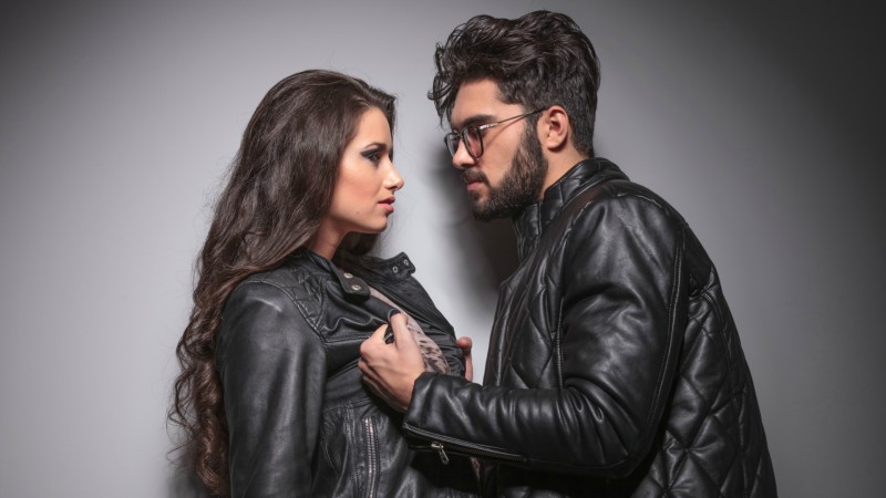 Young fashion couple face to face, the man is pulling his girlfriend leather jacket.
