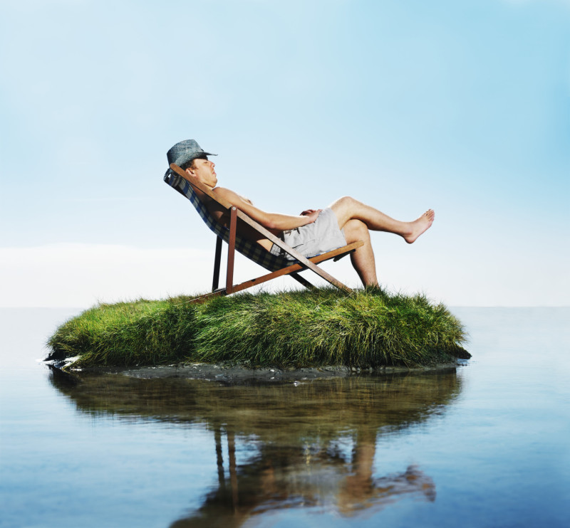 Man sleeping in deckchair on grass island, side view